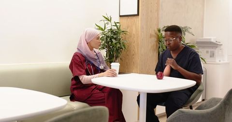 Multicultural healthcare team taking break and talking in clinic lounge with coffee