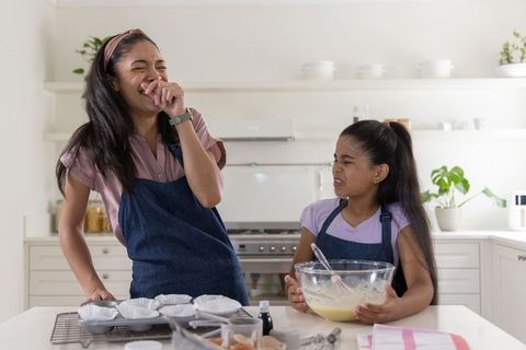 African american mother and daughter laughing while mixing batter in bright home kitchen