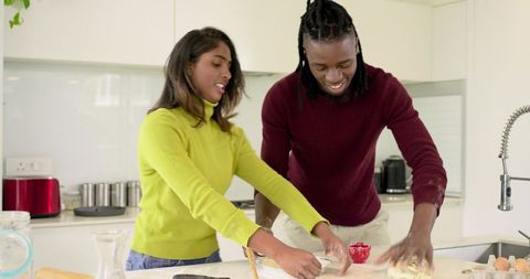 Interracial couple kneading dough together in bright modern kitchen baking homemade bread