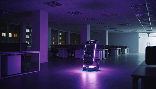 Autonomous cleaning robot glowing purple leds gliding through empty modern office at night