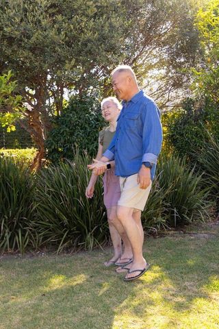Senior asian couple walking hand in hand in sunny backyard garden enjoying companionship