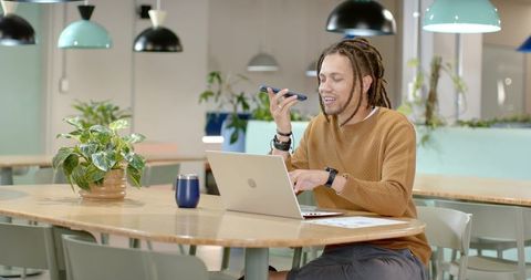 African American man working remotely in bright coworking hub speaking into smartphone