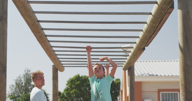 Boy playing on monkey bars while father watches in park. Capture joyful outdoor activity and family bonding moment. Great for promoting children's activities, outdoor fun, and parental interaction.
