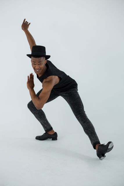 Male dancer wearing black hat and outfit, striking a dynamic pose in a dance studio. Ideal for use in articles or advertisements related to dance, fitness, performing arts, and modern dance techniques. Can also be used for promoting dance classes, workshops, and dancewear.