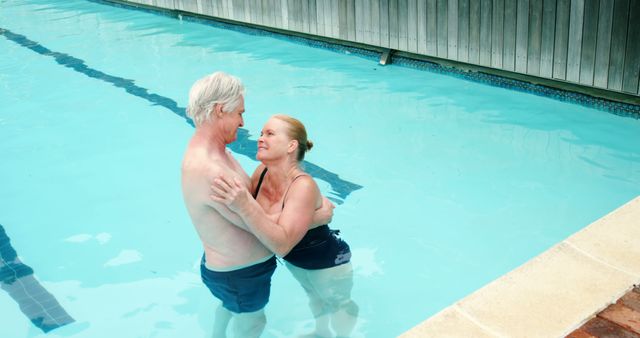 Senior couple standing in a swimming pool, holding each other and smiling warmly. Captures tenderness, love, and the essence of enjoying life even in later years. Ideal for use in advertisements and articles about active aging, retirement living, or senior wellness activities.