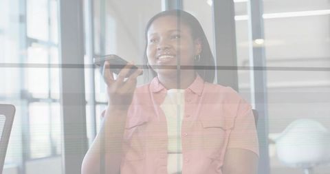 Woman speaking into smartphone while holding phone in modern glass office workspace