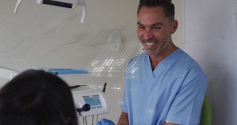 Smiling dentist in blue scrubs interacting with patient during dental exam, clinical care