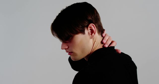 A young Caucasian male appears to be experiencing neck pain or discomfort, with copy space. His expression and posture suggest a sense of unease or physical strain.