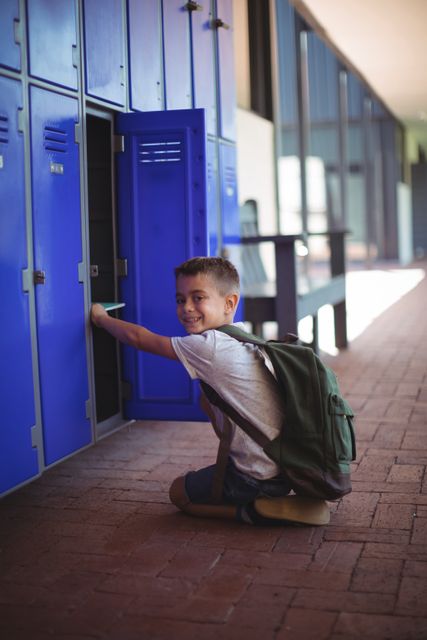 Boy taking books from locker in school corridor, smiling while wearing backpack. Ideal for educational materials, back-to-school promotions, and articles on student life.