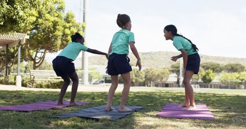 Teen girls practicing yoga and stretching on mats in park wearing school uniform polos