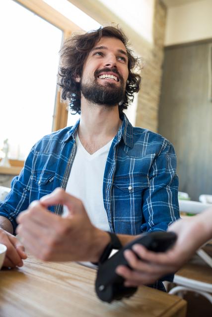 Smiling man using smart watch for express pay at table