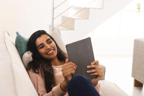 Asian woman relaxing and smiling while using tablet on sofa