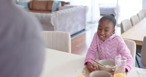Smiling african american young girl eating cereal at family breakfast table in sunlit home