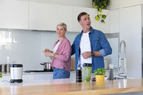 Couple preparing green smoothie in bright modern kitchen laughing and sharing moment