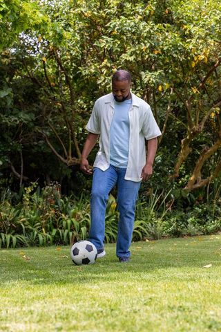 Man playing soccer on lush garden lawn wearing casual jeans and sneakers