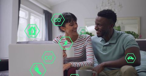 Couple holding mugs viewing laptop with augmented co2 footprint icons in cozy living room