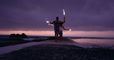 Young couple running with sparklers on beach pier at sunset