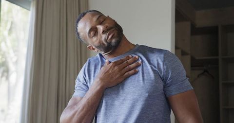 Man practicing deep breathing and chest relaxation at home wearing casual tee