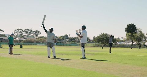 Batsman raising bat celebrating half-century on sunlit suburban cricket pitch