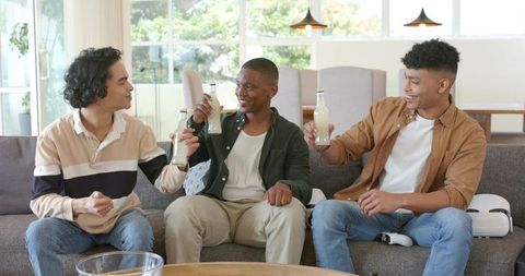 Friends Toasting Bottles on Sofa with VR Headset in Bright Living Room Casual Gathering