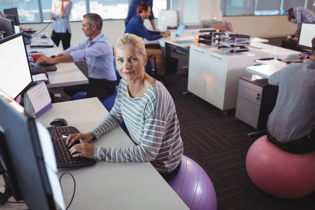 Portrait of businesswoman working at desk while sitting on exercise ball in office
