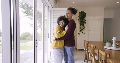 Diverse couple embracing by sliding glass doors in sunlit openplan home