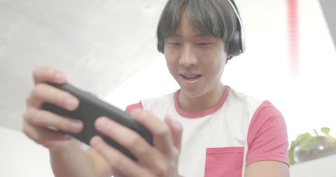 Young man holding smartphone in landscape playing mobile game while wearing headphones