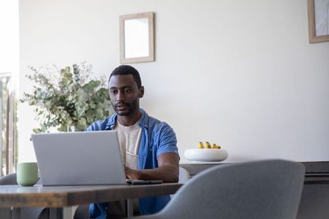 African american man working on laptop in modern minimalist home office, cozy productive