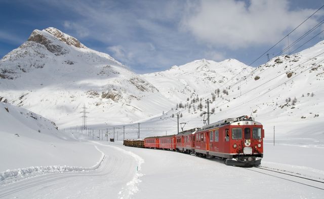 Red train navigating through alpine snowy landscape, showcasing winter travel and scenic beauty. Ideal for content related to travel, Swiss tourism, winter adventures, railway journeys, and alpine scenery.
