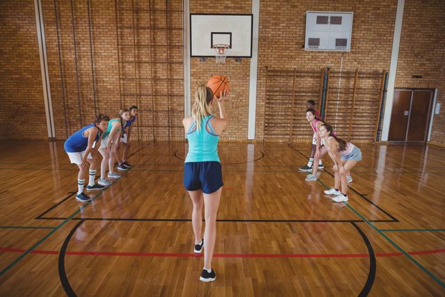 High school girl preparing to take a penalty shot during a basketball game in a gymnasium. Other players are lined up on either side, ready to rebound. Ideal for use in educational materials, sports training guides, youth fitness promotions, and team-building advertisements.