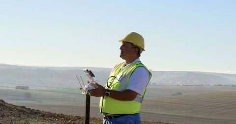 Engineer operating drone in field with wind turbine in background
