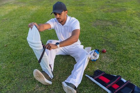 Indian cricketer fastening leg pad on turf, preparing for match in white kit, focused