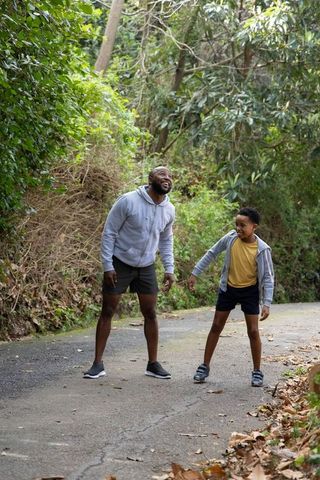 African american father and son walking and laughing on shaded forest trail