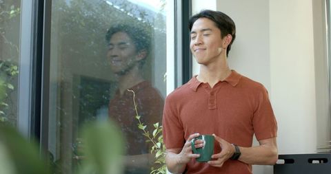 Man enjoying quiet moment indoors holding coffee mug by window