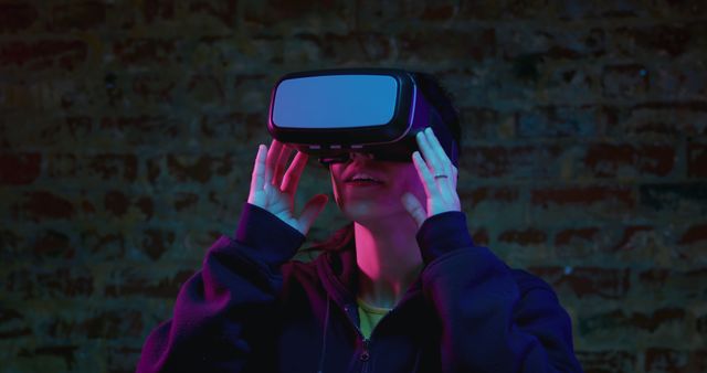 A young Caucasian man is seen engaging with VR technology indoors, his face illuminated by vibrant neon lights. This visual representation is perfect for conveying themes of modern innovation, immersive technology, and futuristic experiences. Ideal for use in blog posts, tech magazines, advertisements for VR products, and articles focusing on the advancement of virtual reality.