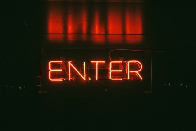 Glowing red neon sign displaying 'Enter' in all caps against a dark background. Perfect for use in design projects related to nightlife, bars, clubs, vintage or retro themes, urban culture, and electric signboards. Suitable for advertisements, social media graphics, website banners, and promotional materials for nightclubs and entertainment venues.