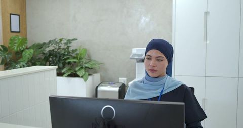 Professional female receptionist wearing navy hijab working at modern minimalist reception desk