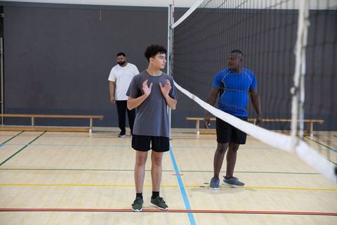 Young diverse men practicing volleyball indoors on hardwood court during team training