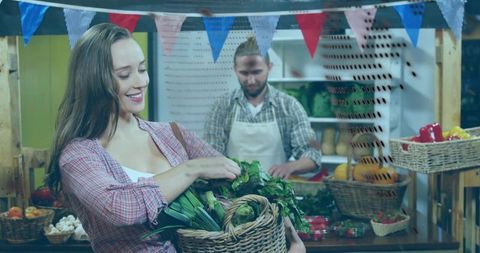 Smiling woman picking greens from woven basket at vibrant farmers market with vendor in background