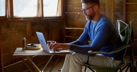 Man Using Laptop in Cozy Wooden Cabin Workspace