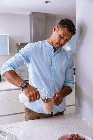 Man pouring milk into mug in minimalist kitchen