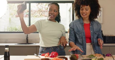 Diverse female friends filming recipe video while preparing avocado bowl in bright kitchen