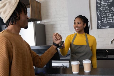 African american customer tapping smartwatch for contactless payment in cozy cafe
