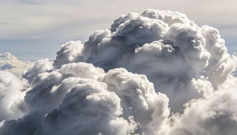 Billowing cumulonimbus towers catching sunlight over layered atmospheric clouds