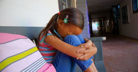 Sad Schoolgirl Sitting Alone on Bench in School Corridor