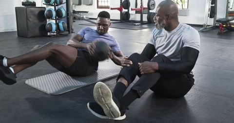 Trainer Guiding Client in Medicine Ball Exercise at Gym