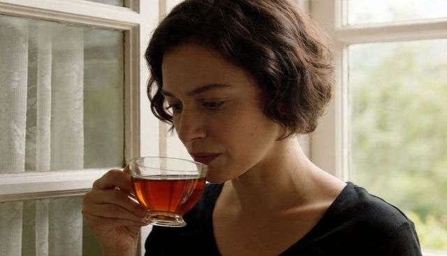 Woman sipping tea in glass cup by window contemplative sunlit portrait minimalist lifestyle