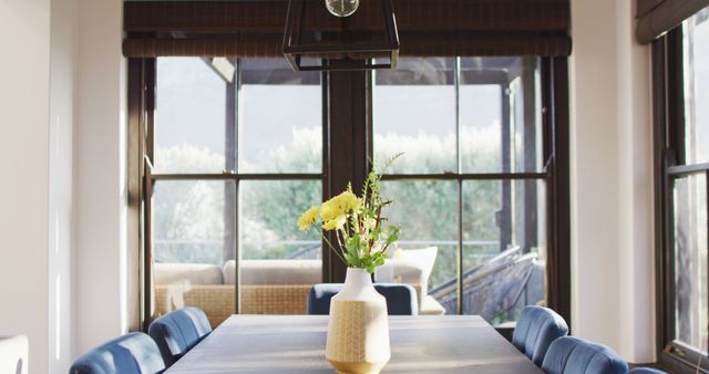 Elegant dining room featuring a modern table with fresh flowers in the centerpiece. The room is filled with natural light from large windows, highlighting the minimalist decor. Perfect for content about home decor ideas, contemporary interior design, or lifestyle features.