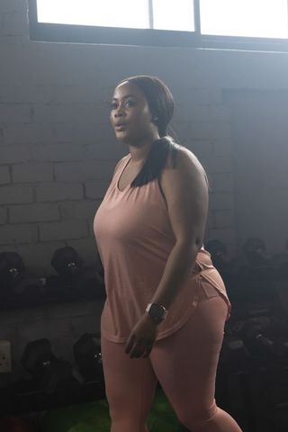 African american woman training by dumbbell rack in pink activewear wearing smartwatch