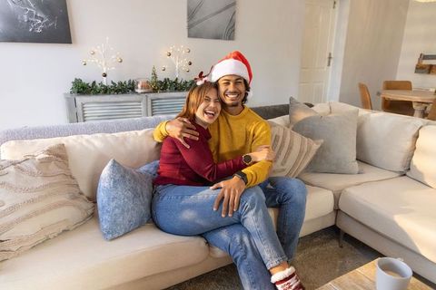 Couple hugging on sofa wearing santa hat and cozy sweaters celebrating christmas morning